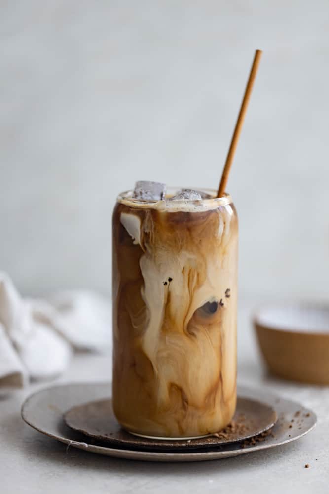 Iced coffee with a straw in a glass on a light surface