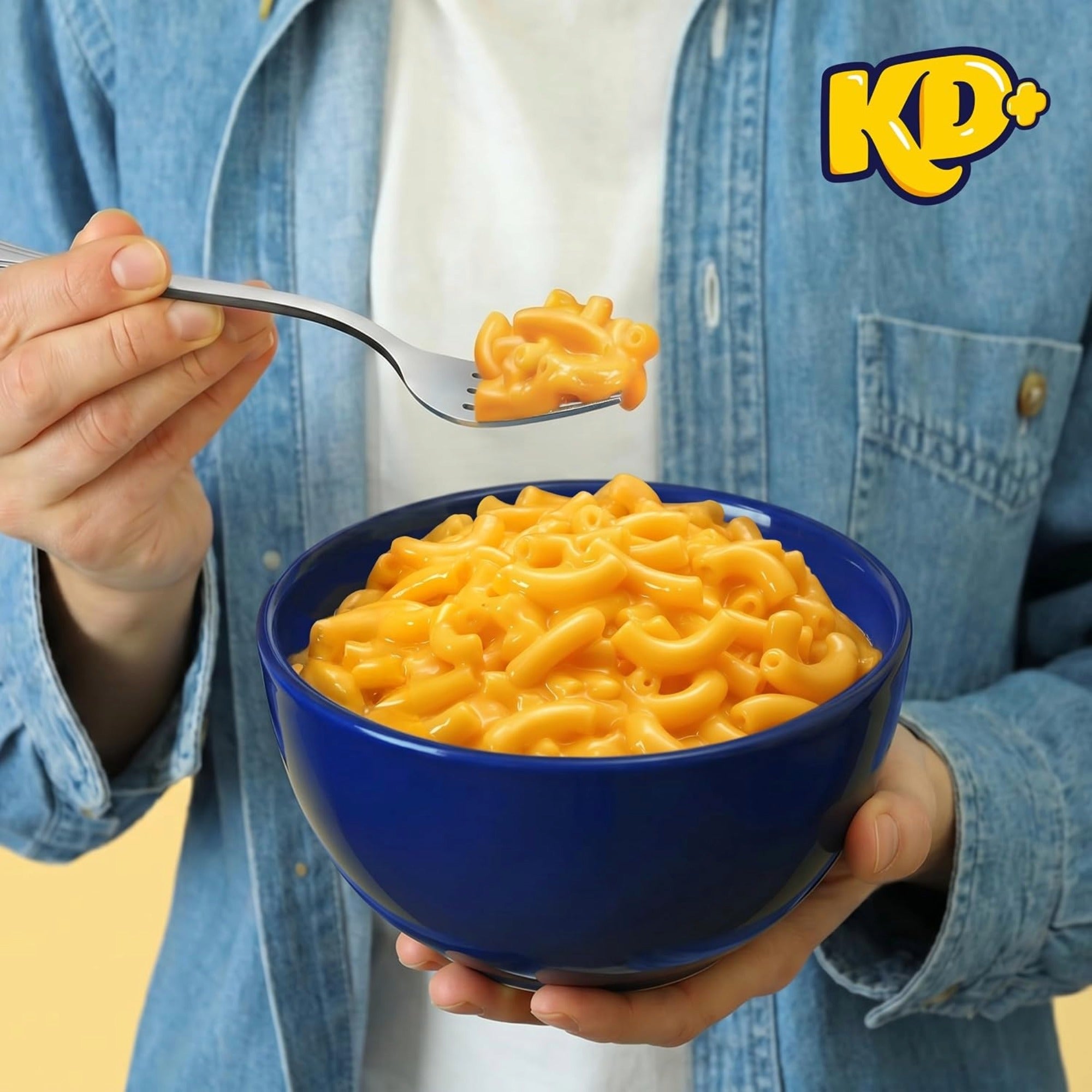 Person holding a blue bowl of KD+ Original macaroni and cheese and lifting a forkful.