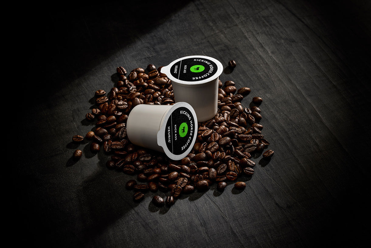 Two coffee pods with a green logo on a bed of coffee beans on a dark surface