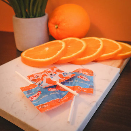 Kerr's COUGH & Sore Throat Lollypop Orange Lozenges laying on a wood and marble cutting board with an orange and orange slices 