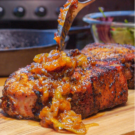 Juicy grilled pork loin seasoned with Kinder's Wood-Fired Garlic dry rub, topped with caramelized onion glaze on a cutting board