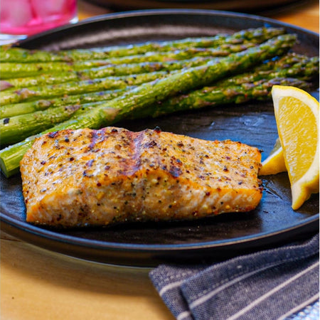 Pan-seared salmon fillet seasoned with Kinder's Buttery Steakhouse dry rub, served with grilled asparagus and lemon wedge