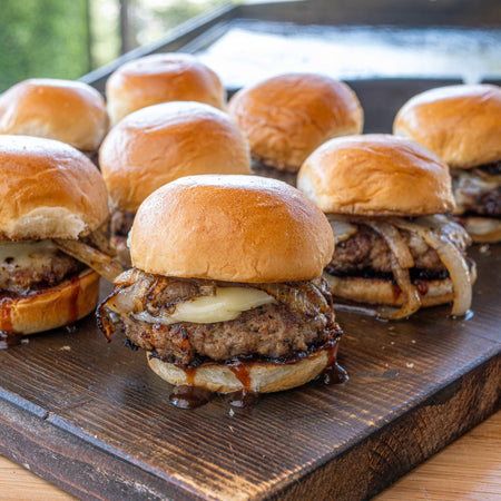 Juicy grilled burgers with caramelized onions seasoned with Kinder's Caramelized Onion Butter dry rub on a wooden board