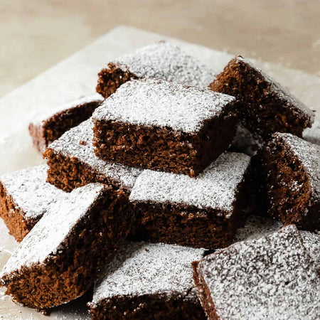 A serving plate with molasses cake dusted with powdered sugar on a light surface