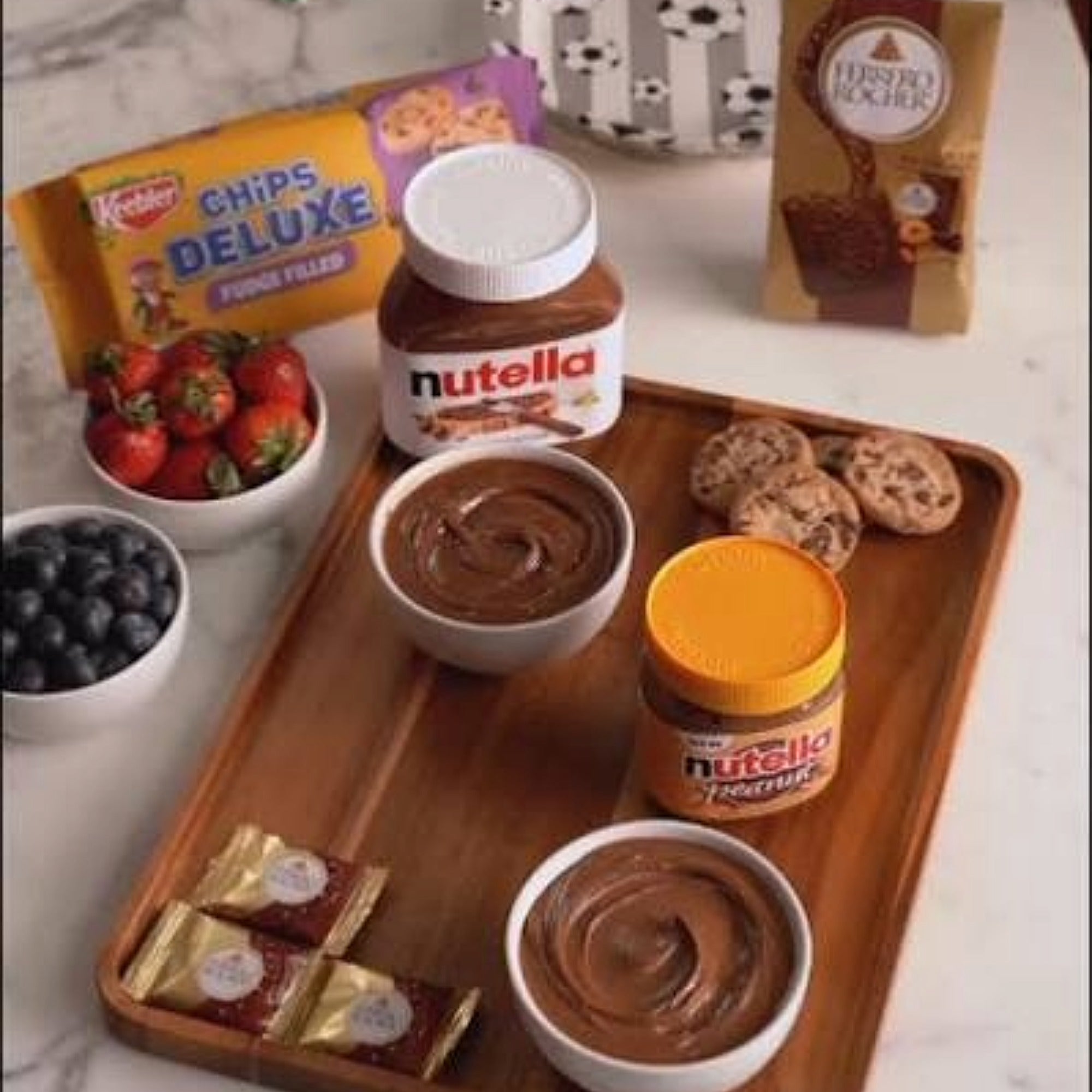 Nutella Peanut Spread 725g on a charcuterie snack board with strawberries, blueberries, cookies, and Ferrero Rocher