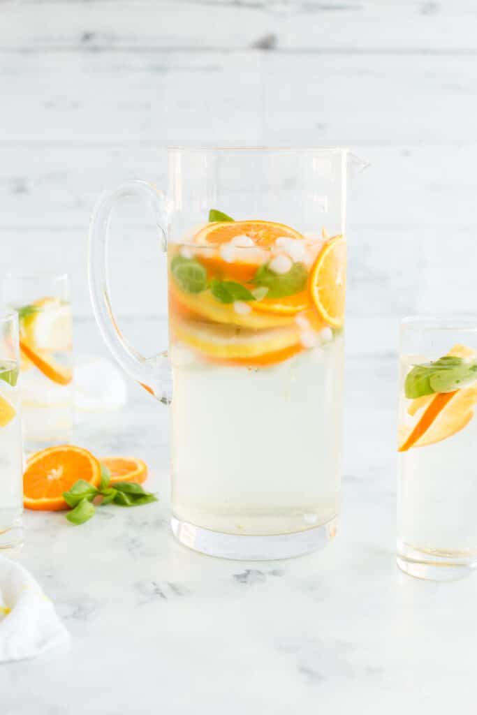 Clear glass filled with a refreshing drink garnished with orange slices and mint leaves on a light marble background.