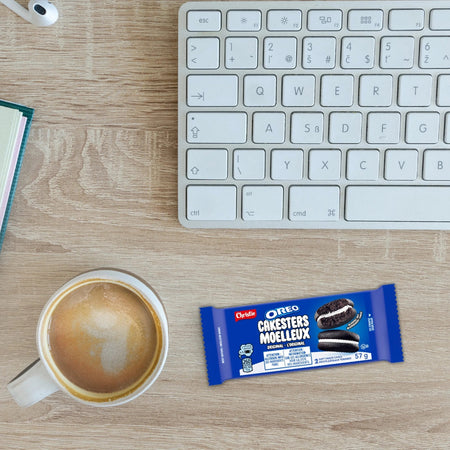 Cup of coffee, Oreo cookie bar package, and keyboard on a wooden desk