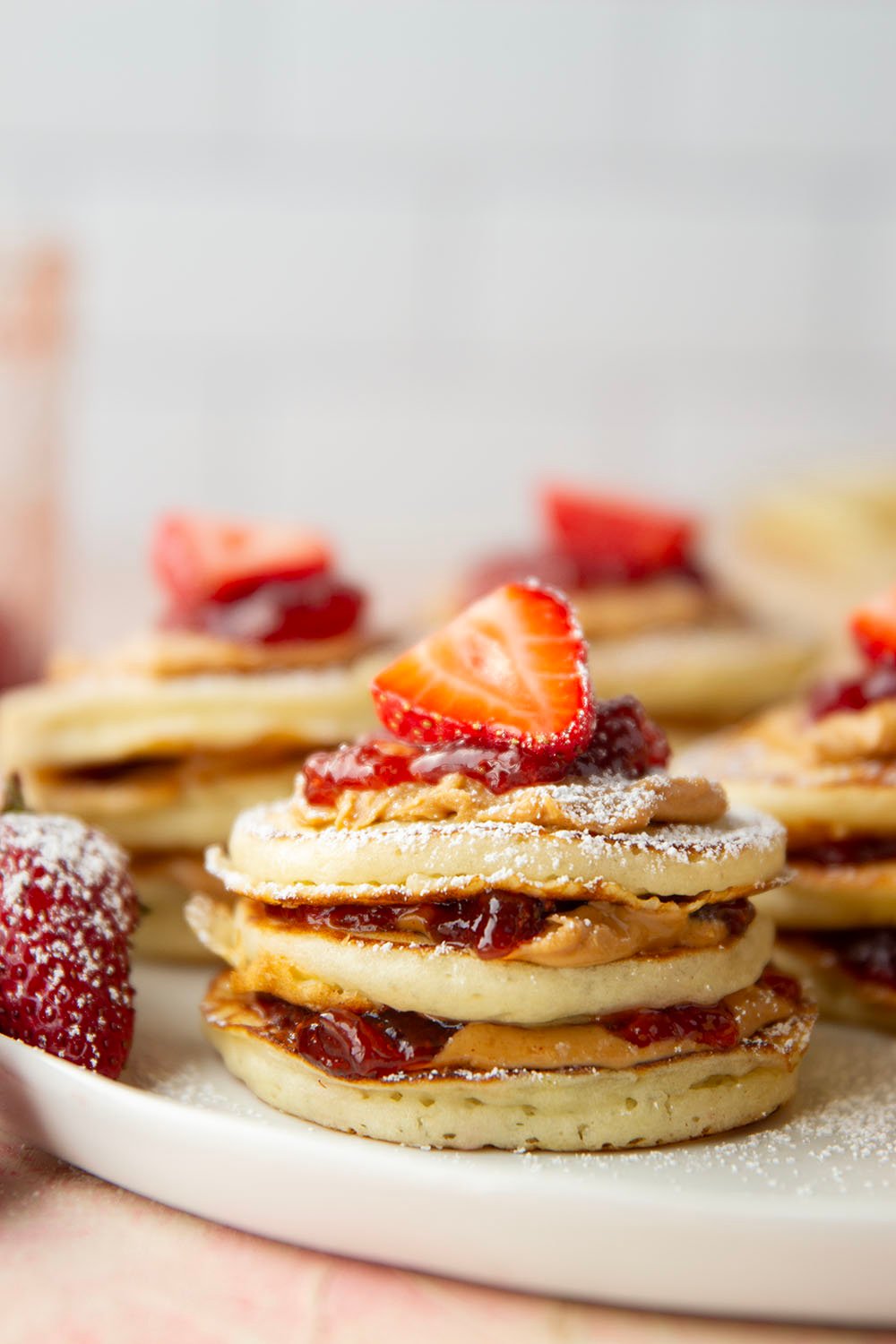 Stack of pancakes with strawberry jam and peanut butter on a white plate