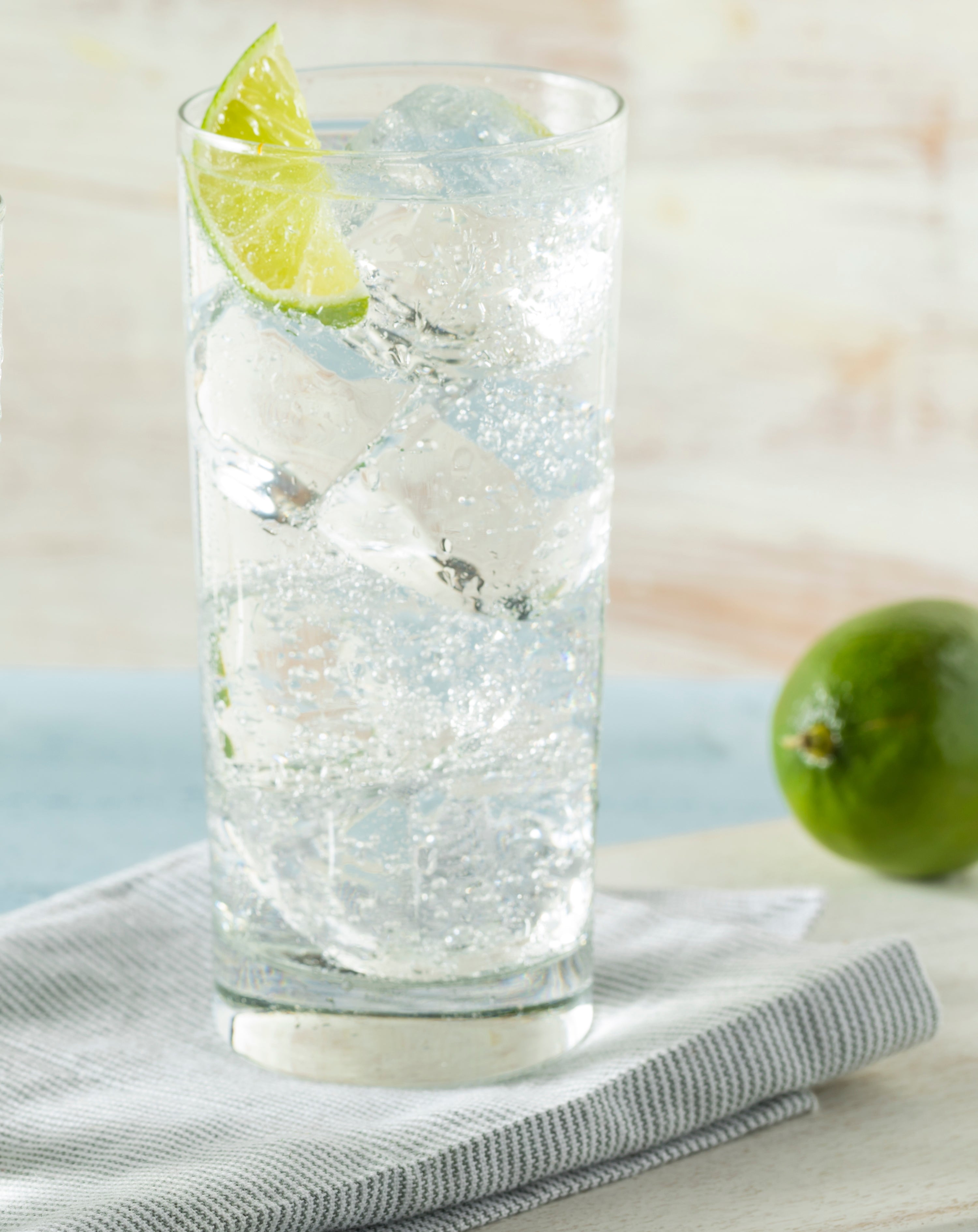 Glass of sparkling water with a lime wedge on a light surface
