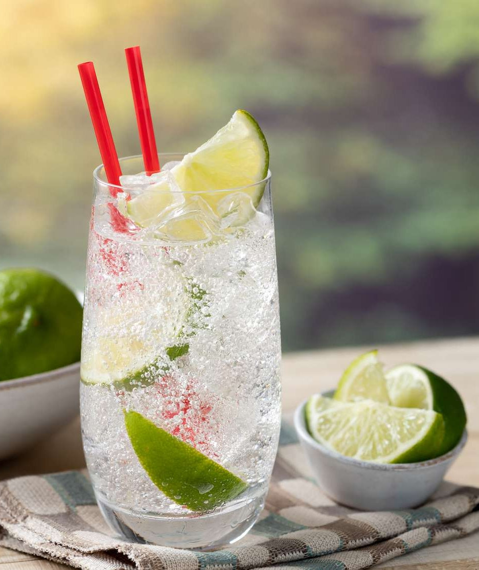 Glass of sparkling water with lime wedges and red straws on a blurred outdoor background