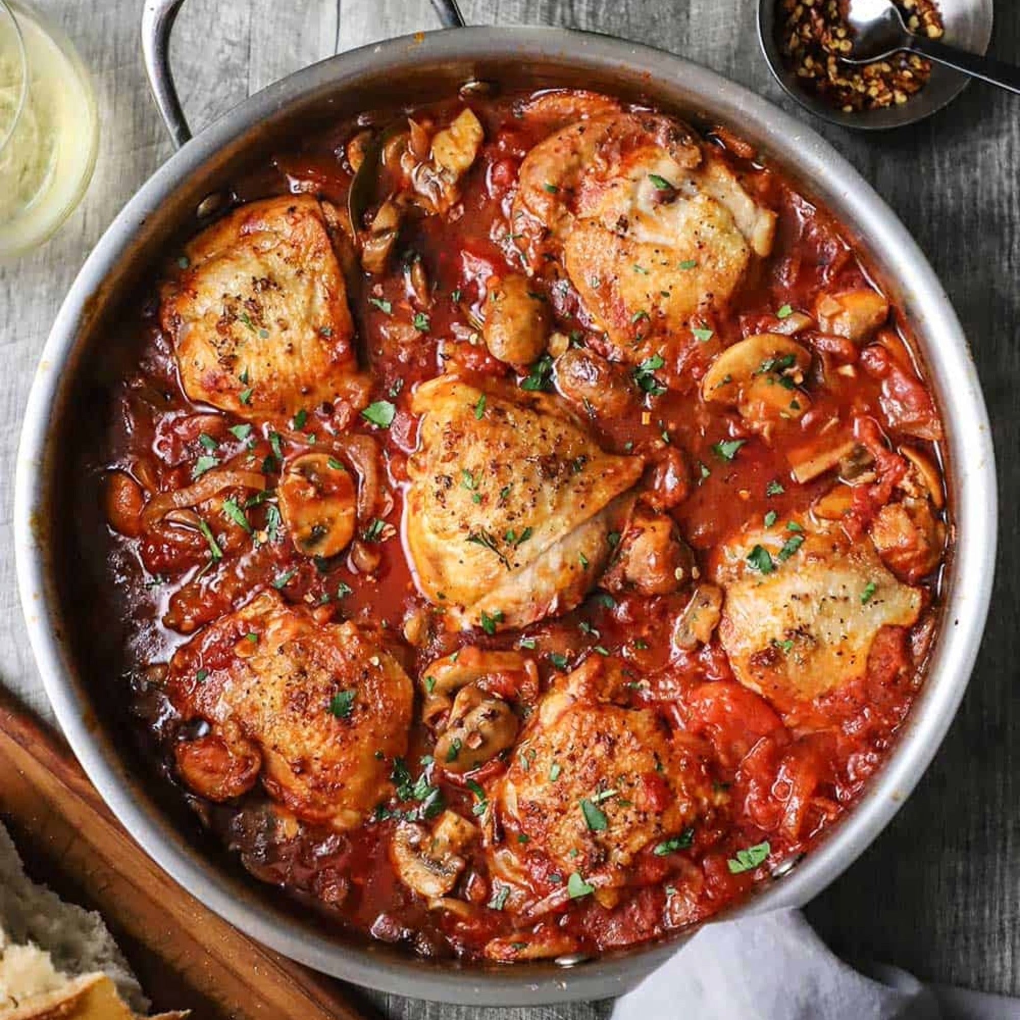 Chicken thighs simmered in tomato cacciatore sauce with sliced mushrooms and chopped herbs in a skillet.