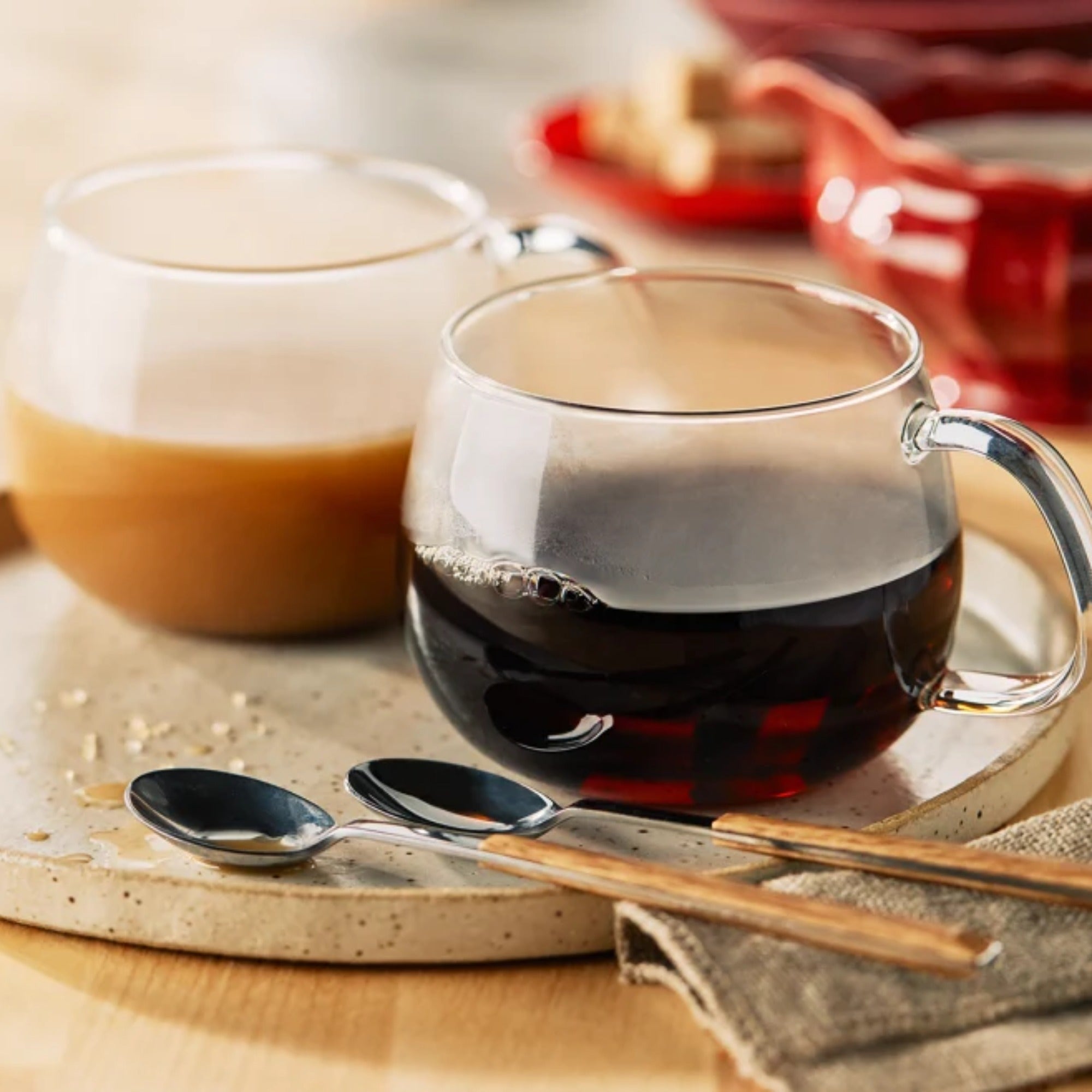 Two cups of prepared maple rooibos tea served original flavor and with added milk on marble stone ware , two spoons, cloth on a wooden surface.