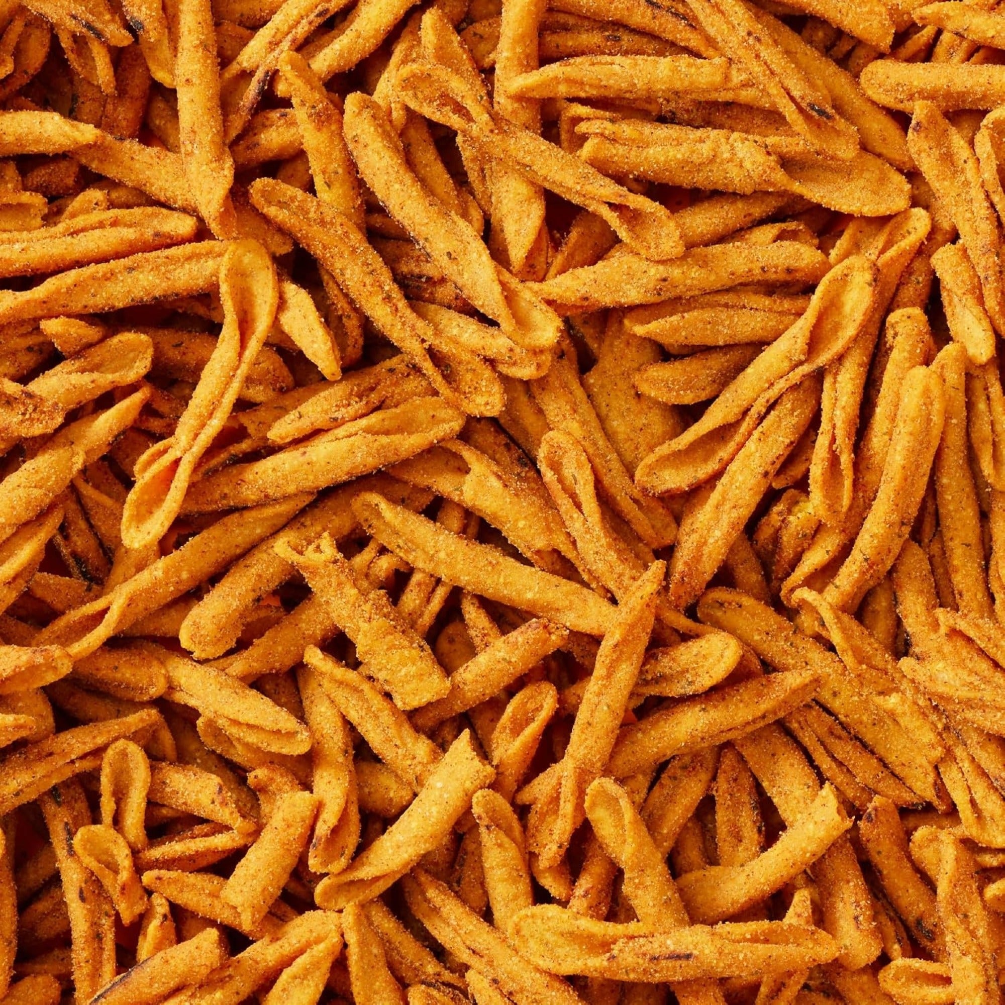 Close-up of golden Que Pasa Organic Spicy Queso rolled tortilla chips coated with seasoning.