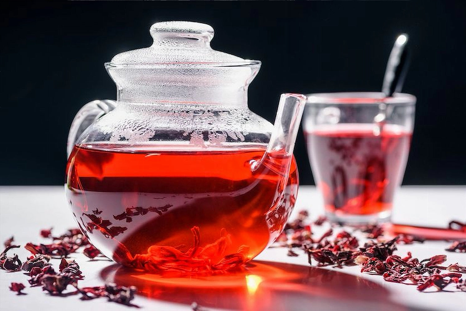 Glass teapot with red liquid and a glass of tea on a dark background