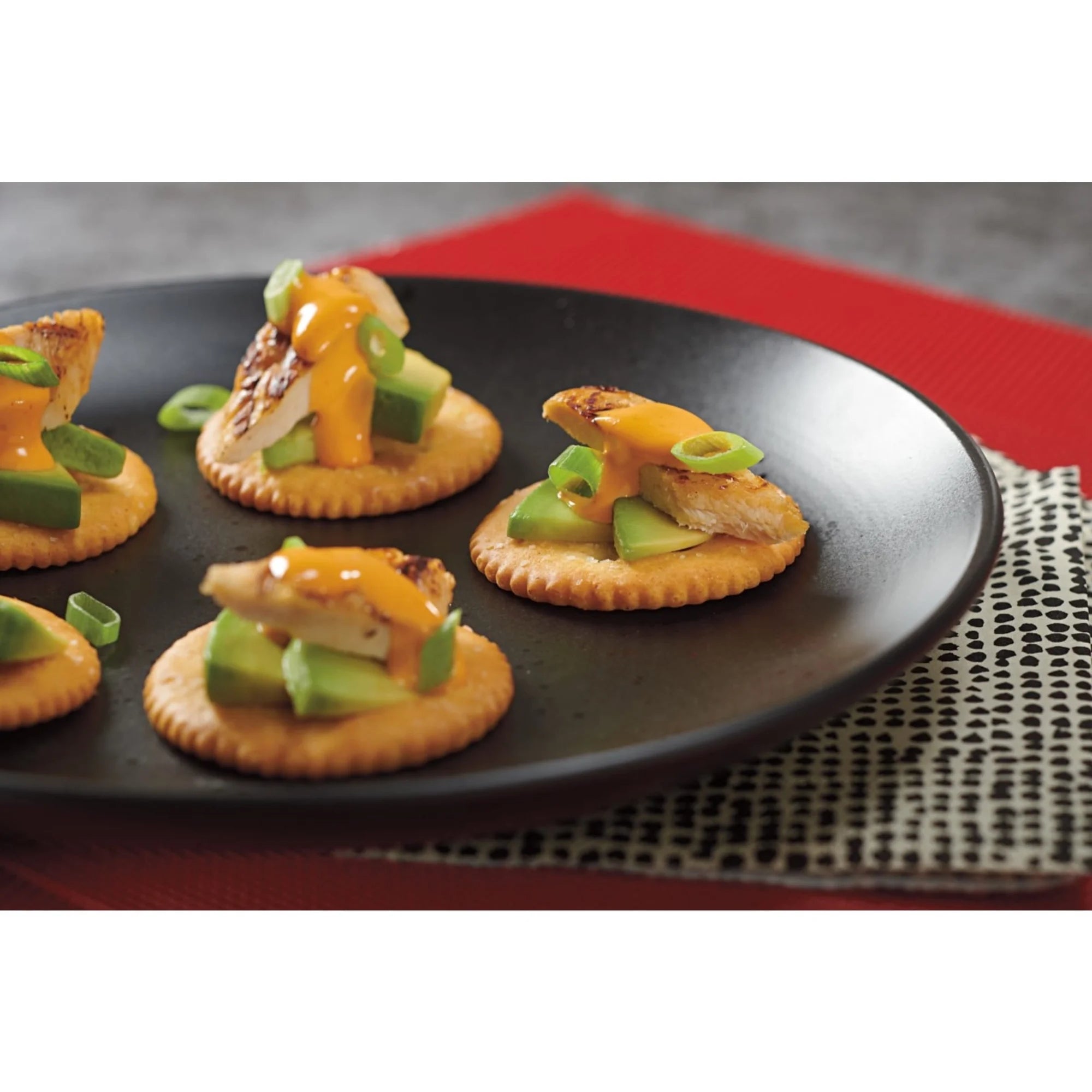 Platter of appetizers with crackers, cheese, and green onions on a black plate.