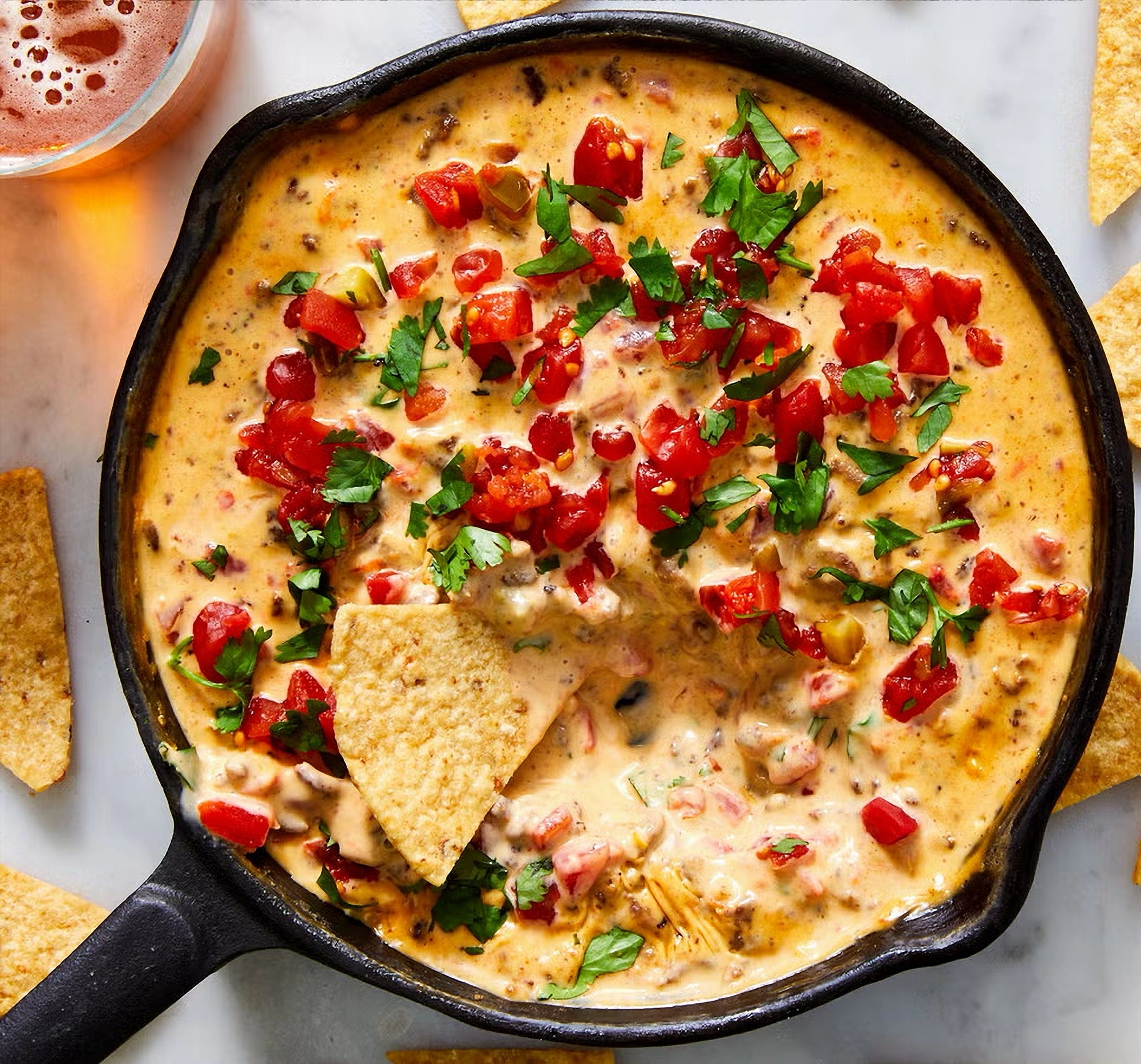 Hot cheese dip with tomatoes and cilantro in a skillet with a tortilla chip dipped into it.