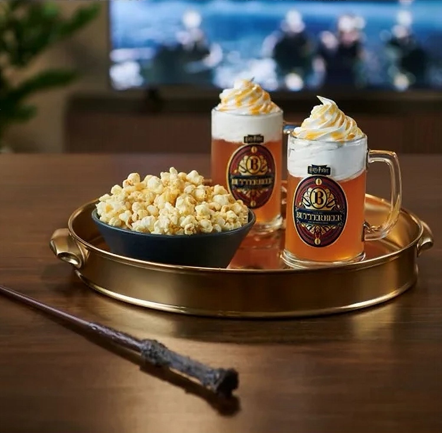 Two mugs of Butterbeer with whipped cream on a tray with popcorn