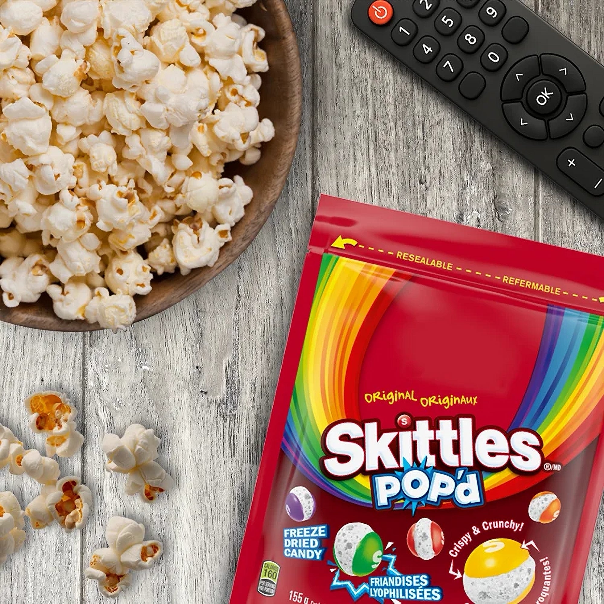 Skittles Pop'd candy package with a bowl of popcorn and remote control on a wooden surface