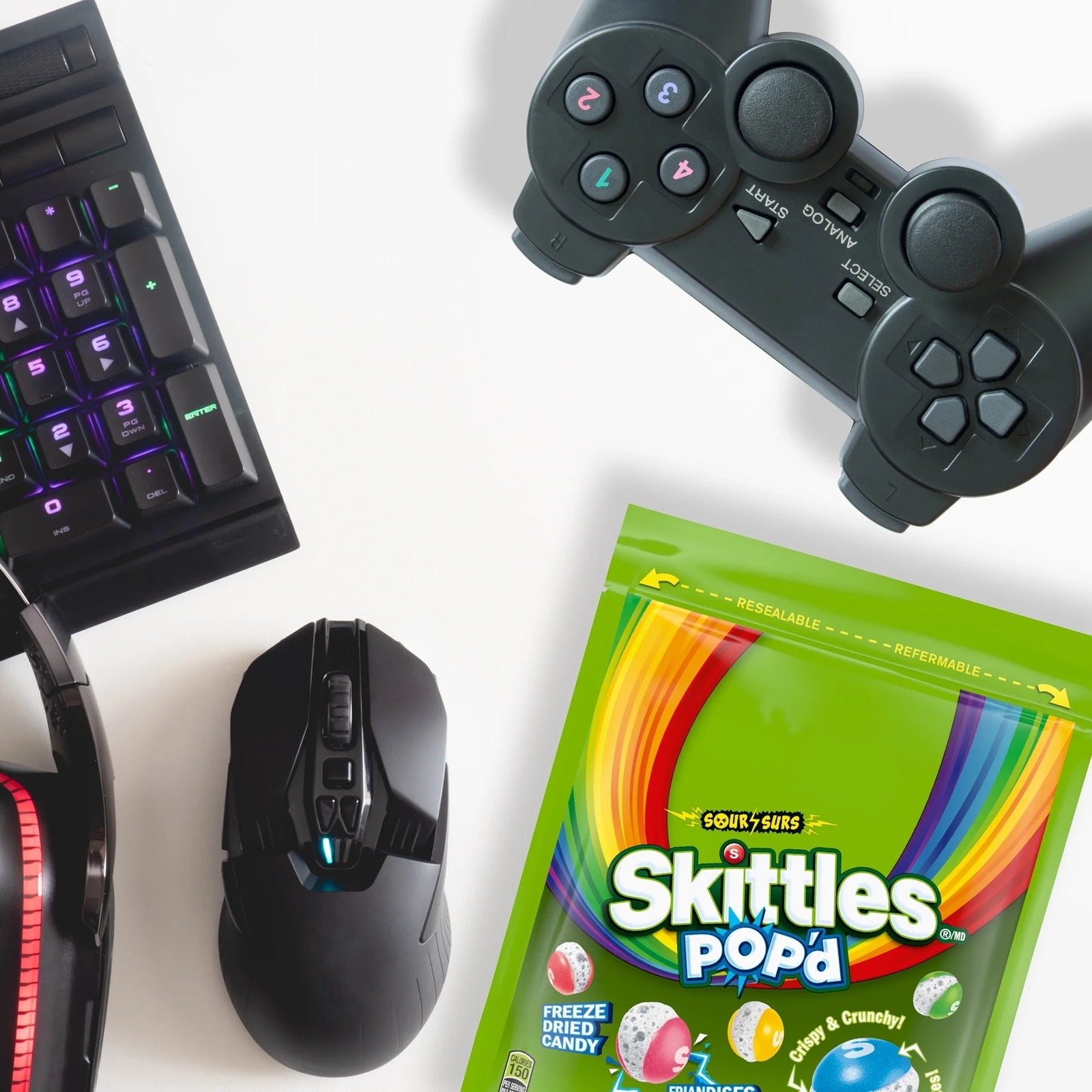Gaming setup with keyboard, mouse, and controller on a white background, featuring a Skittles Pop-a-corn bag.