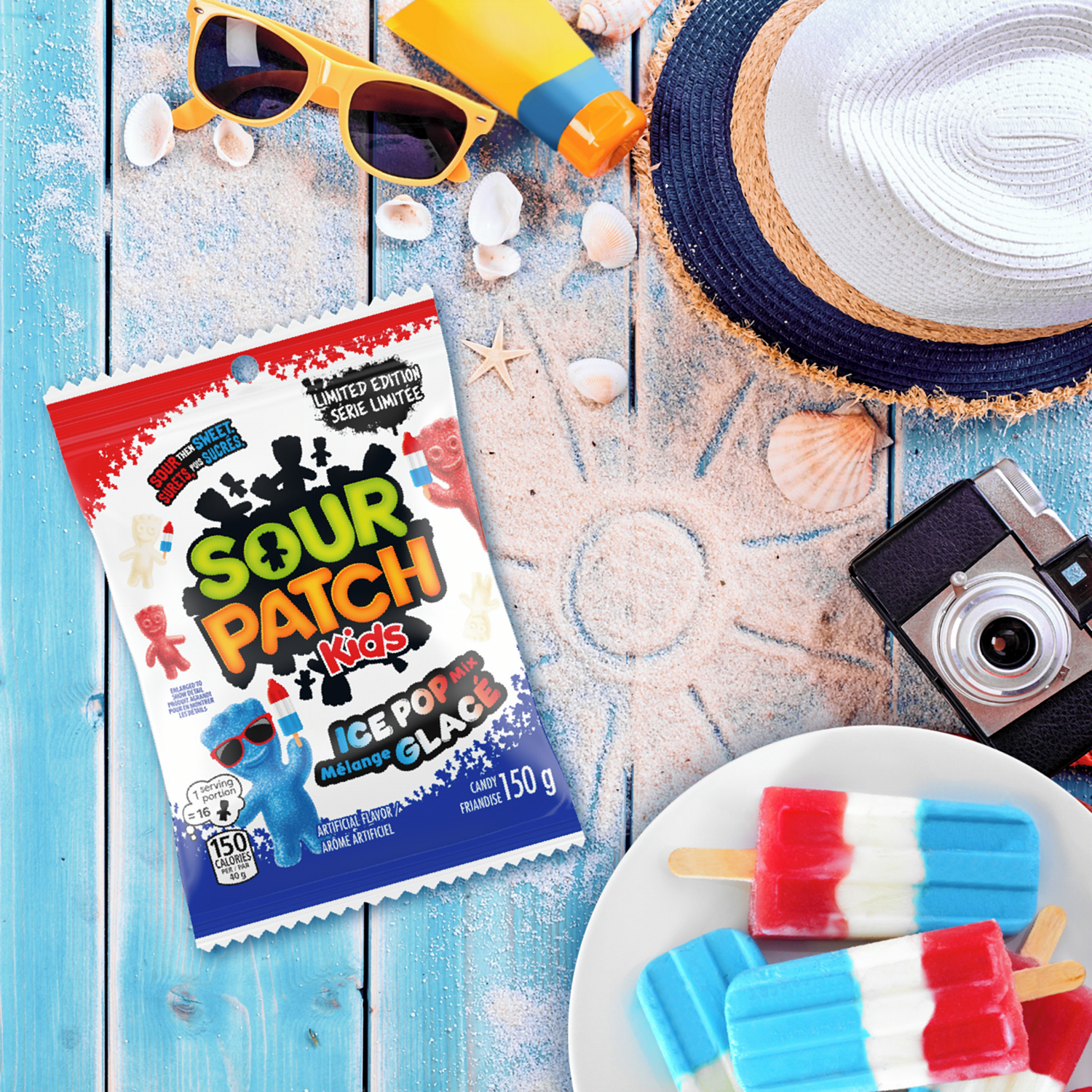 Sour Patch Kids ice pop package with popsicles, sunglasses, and a camera on a wooden surface.