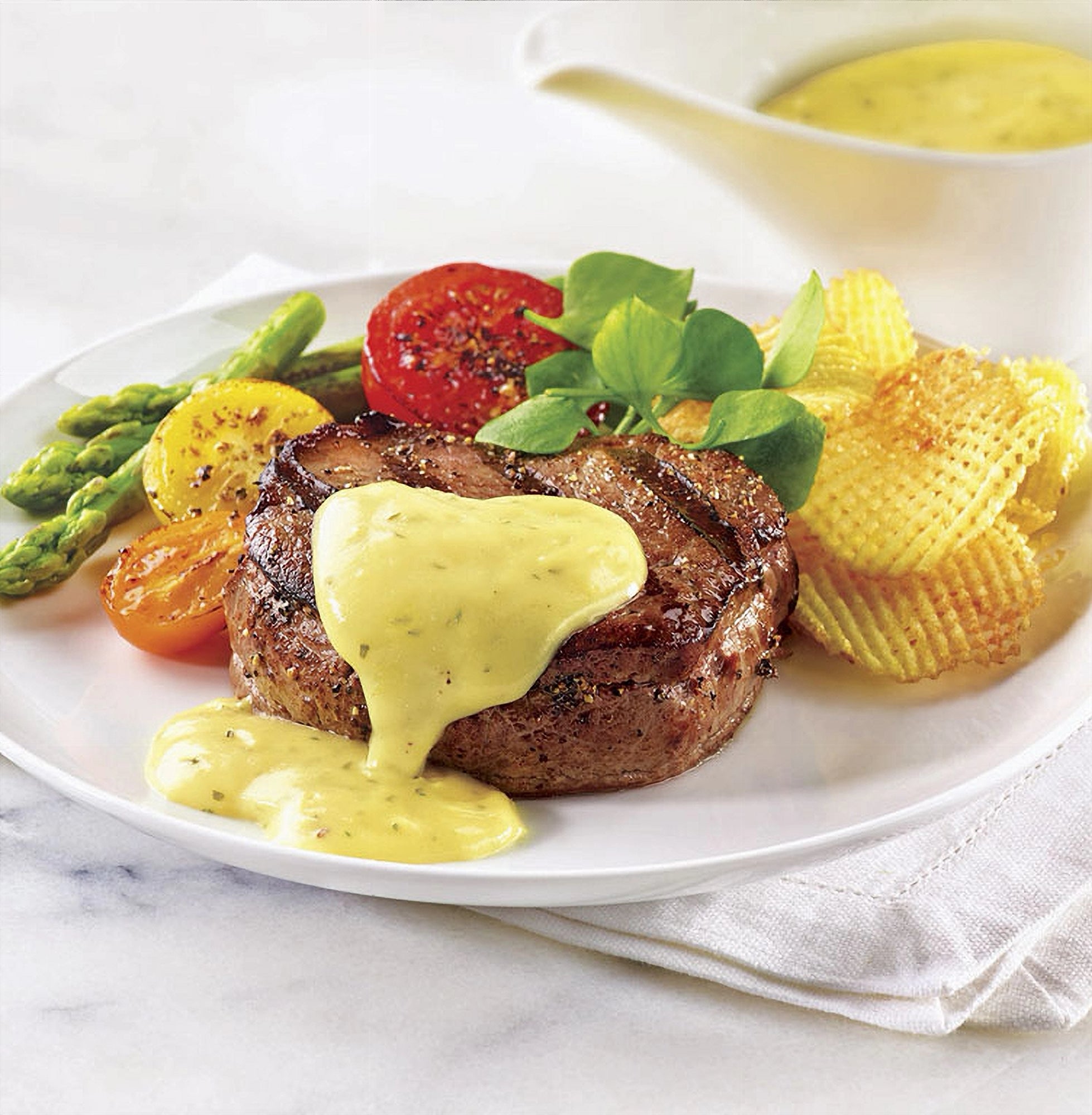 Steak with The Keg Bearnaise Sauce on a plate with vegetables, potato chips and basil