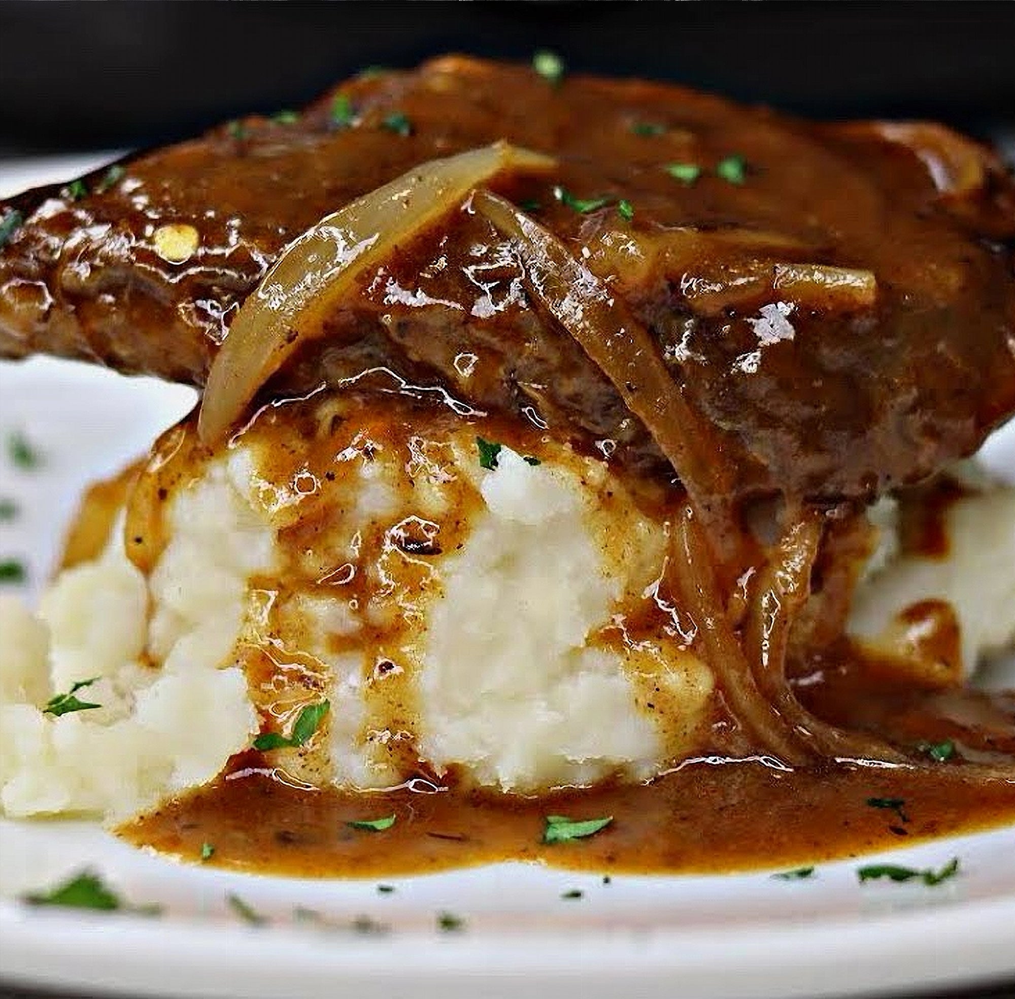 Plated dish of meat with onion gravy over mashed potatoes