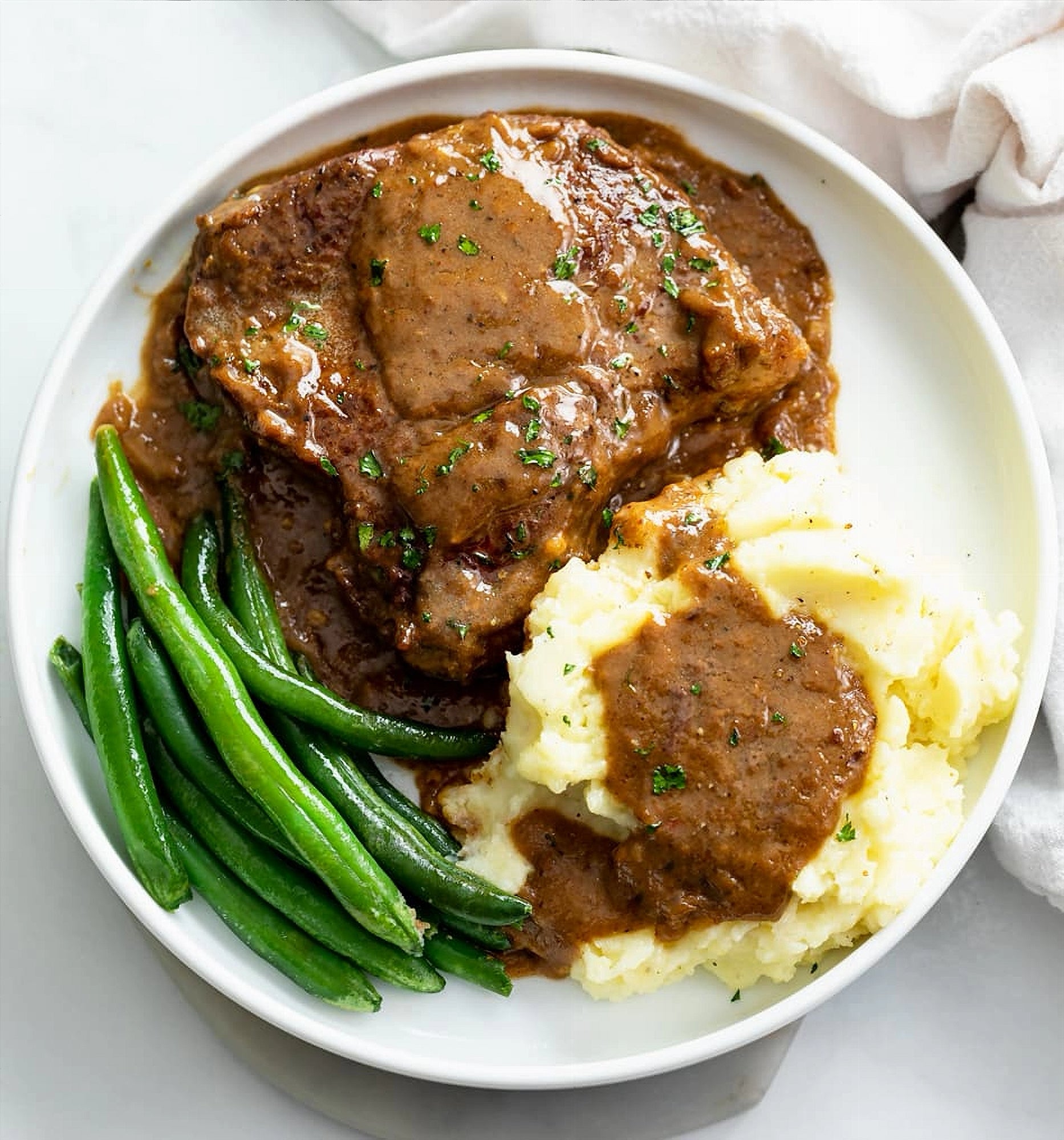 Plated meal with meat, mashed potatoes, and green beans on a white plate.
