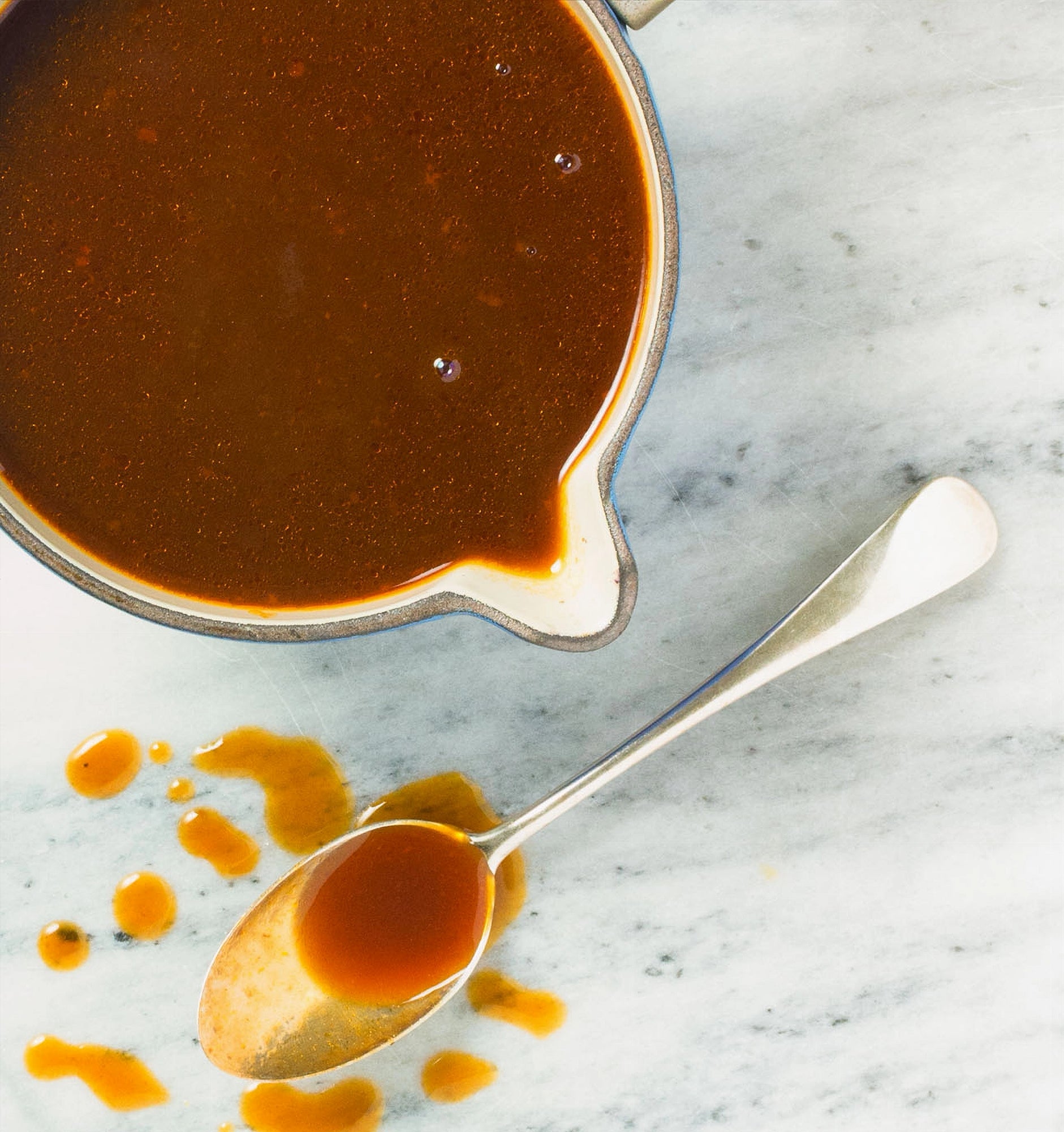 Demi glace glace in a small pot with a spoonful of sauce on a marble surface
