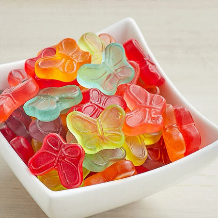 Colorful butterfly-shaped gummy candies in a white bowl on a light background