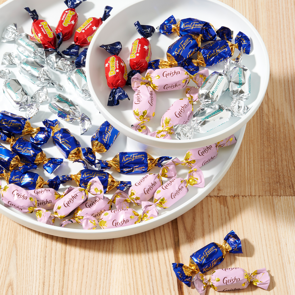 Assorted candies in colorful wrappers on a white plate with a wooden surface.