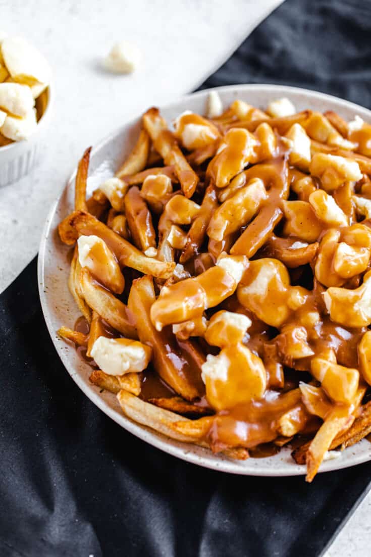  bowl of prepared poutine with fries and cheese curds on a plate on a dark surface