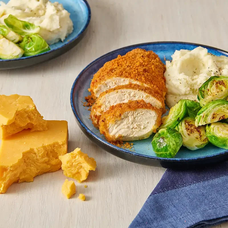 Plated dish of breaded chicken with mashed potatoes and brussels sprouts, accompanied by a block of cheese.