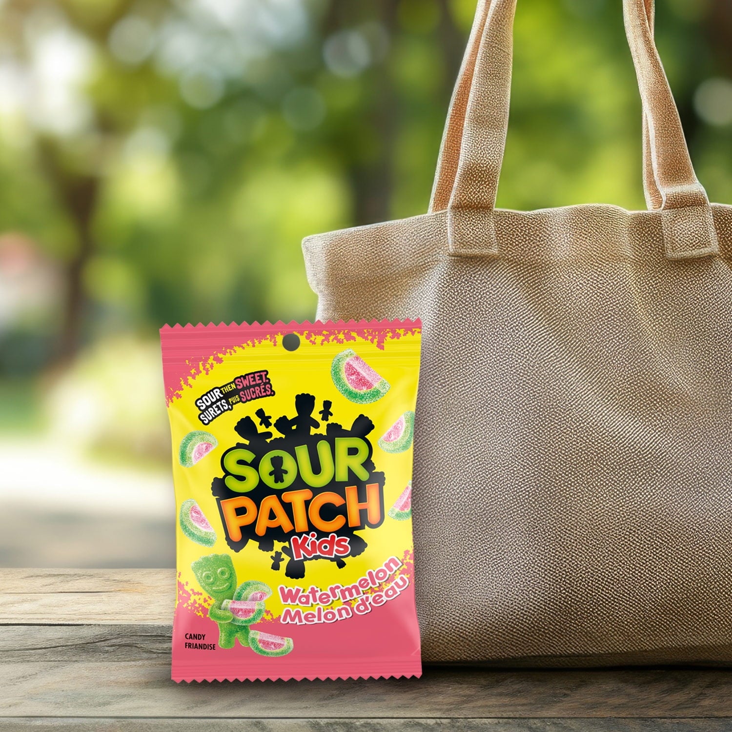 Sour Patch Kids watermelon candy package next to a beige tote bag outdoors.