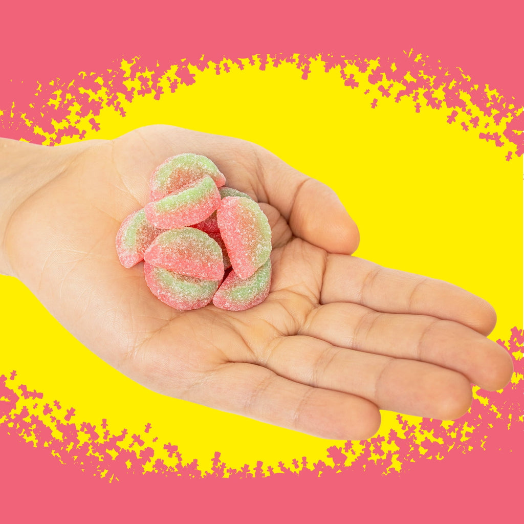 Hand holding pink and green gummy candies against a yellow and pink background