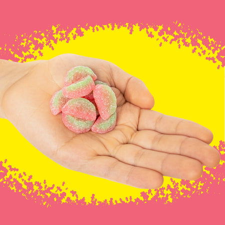 Hand holding pink and green gummy candies against a yellow and pink background