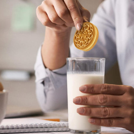 Person holding a glass of milk and an Oreo Brown Sugar Bubble Tea Sandwich Cookie above it.