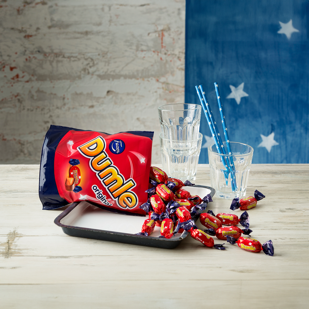 Bag of Dumle candies on a tray with glasses and straws against a rustic wall.