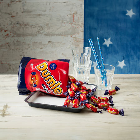 Bag of Dumle candies on a tray with glasses and straws against a rustic wall.