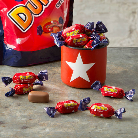 Dumle candies in red and blue wrappers with a Dumle cup on a gray surface.