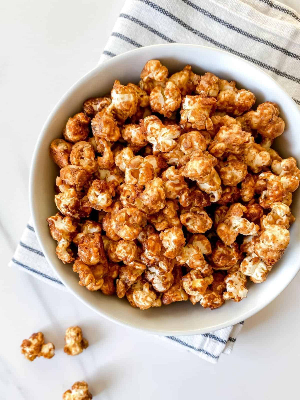 White bowl filled with Compliments Spicy Maple Flavored Popcorn Mix, Sweet & Spicy Popcorn Snack 200g/7.1 oz on a white surface with a striped cloth.