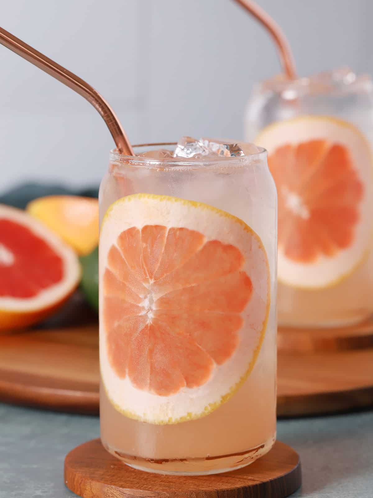 Glass of pink grapefruit cocktail with a slice of grapefruit on a wooden coaster.