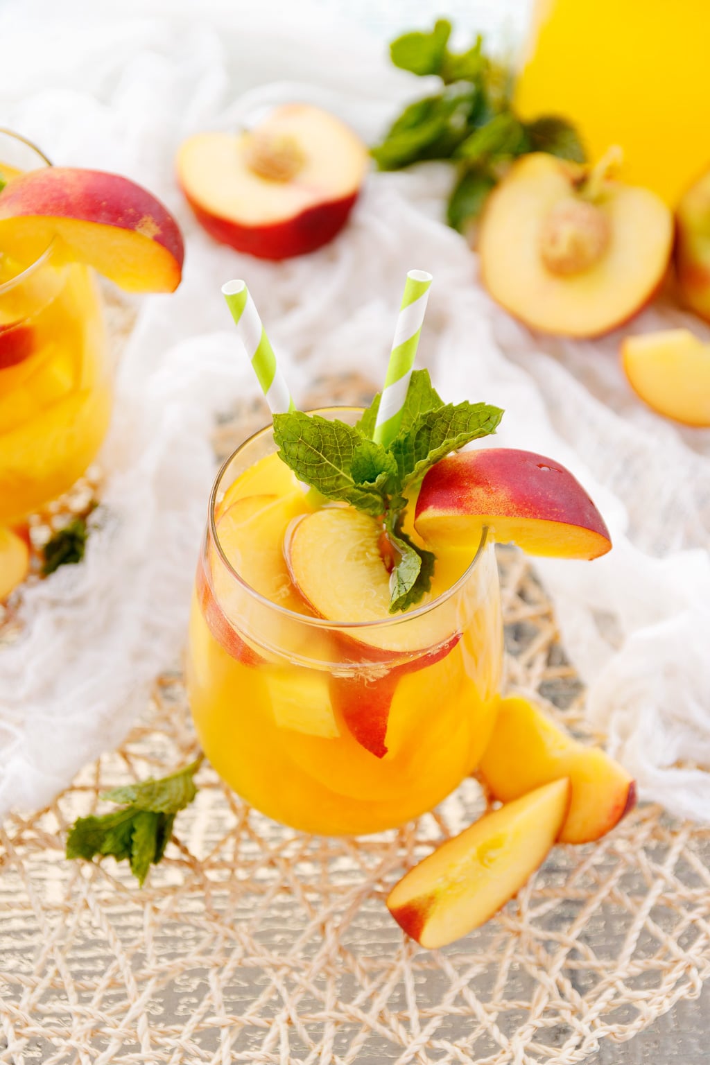Glass of peach sangria with peaches and mint leaves on a white lace tablecloth.