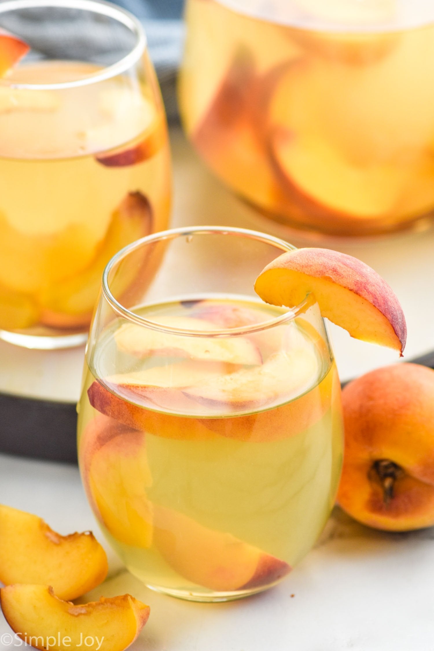 Glass of peach-scented drink with peach slices on a white surface