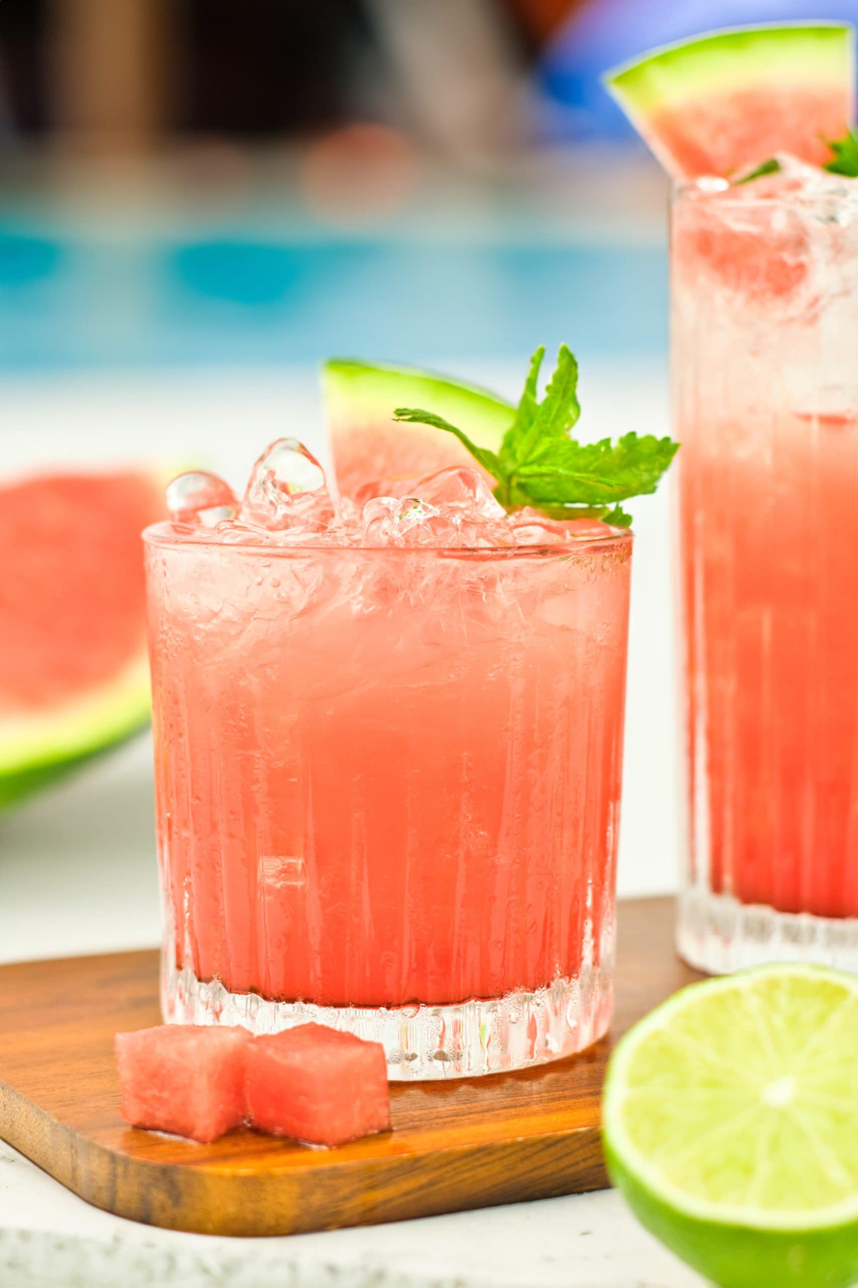 Two glasses of watermelon juice with watermelon slices and lime on a wooden board.